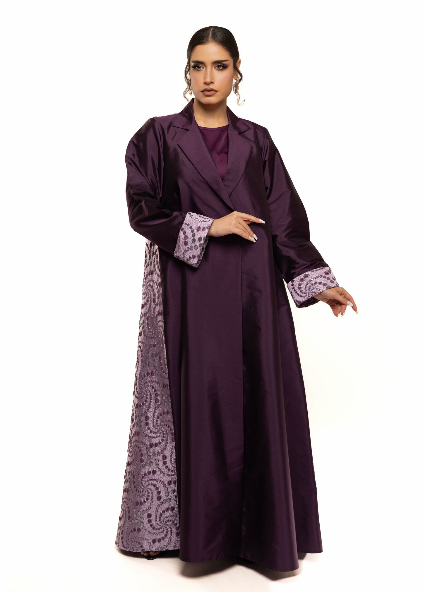 Woman wearing a long purple dress with patterned trim on a white background